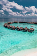  Stunning summer aerial landscape of Maldives water villas over pristine turquoise sea, luxury resort under sunny blue sky with scattered clouds, perfect tropical vacation and tourism destination