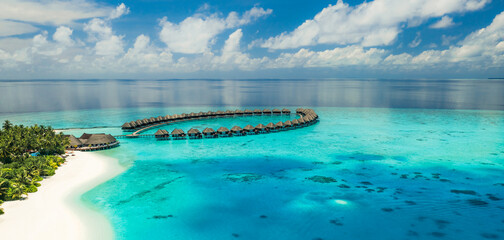 Stunning summer aerial landscape Maldives water villas pristine sea lagoon, sunny blue sky clouds perfect island shore. Beautiful palm trees tropical paradise vacation tourism luxury resort escape