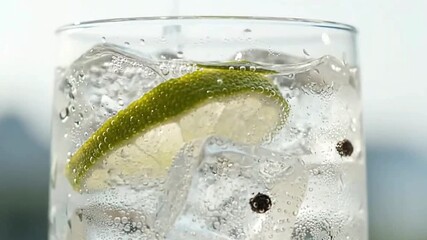 A chilled drink in a clear glass with ice lime slice and bubbles suggesting gin and tonic or a similar cocktail - Powered by Adobe