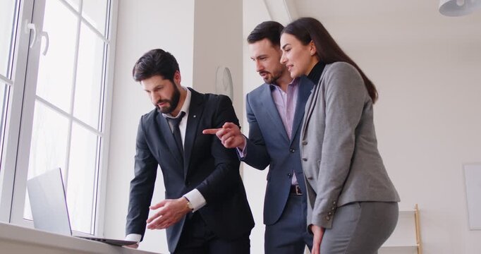 Couple discussing possible deal with real estate agent while meeting in new apartment for house tour. Husband and wife talking to advisor, looking at laptop, and choosing mortgage loan offer - Powered by Adobe