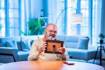Elderly Indian man holding framed photo with love, lost in memory and emotion