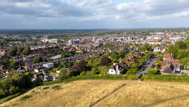 Aerial view of rooftops and buildings merging with green spaces, with the iconic Mount standing prominently, Guildford, England, United Kingdom.
