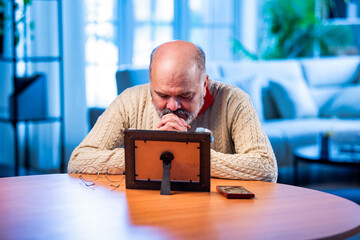 Elderly Indian man holding framed photo with love, lost in memory and emotion