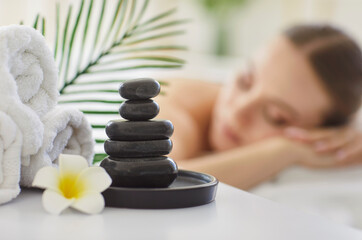 Serene spa set, rolled towels, stack of smooth hot stones, asian flower, woman lying relaxed with...
