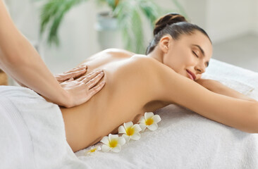 Young woman enjoying relaxing soothing back massage in spa, breathing aroma from flowers, lying on...