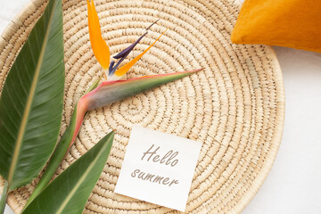 Wicker tray, strelitzia flower and leaves, colored decorative pillows, card with text HELLO SUMMER....