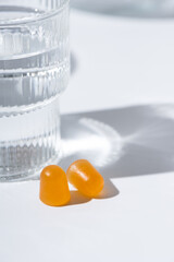 Vitamin gummies pills and Glass cups and a jug of clean, clear drinking water stand on a white tabletop. Sunny day and sharp shadows from glass