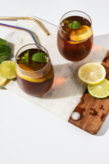 Glass cups and a jug of lemon and lime iced tea on a white table. Sunny day and sharp shadows from glass of lemonade