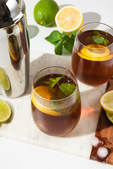 Glass cups and a jug of lemon and lime iced tea on a white table. Sunny day and sharp shadows from glass of lemonade