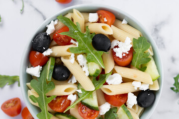 Mediterranean Pasta Salad in bowl with Fresh Vegetables and Herbs on white marble background