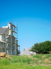 Chimney-focused construction site in Dallas, Texas with pitched roof installed. Unfinished walls and scaffolding showcase multistory home building phase against vivid sky and green foreground
