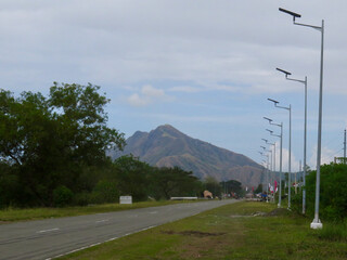 Road to the mountains. Asphalt road and lamp posts. View of highway and lamp posts along the road on flat terrain with mountain on horizon.
