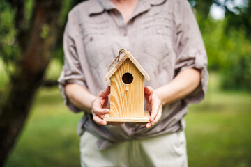 Woman holding small handmade wooden birdhouse in garden, ready to hang on tree
