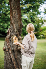 Woman looks at tree where hang birdhouse. Supporting birds and nesting in garden