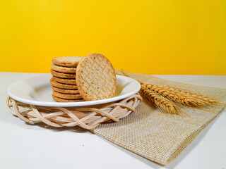 A pile of whole wheat biscuits or healthy crackers on a plate, isolated on a yellow background and...