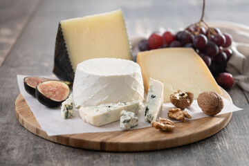 Board of different cheeses with nuts, figs, grapes and wine on wooden table