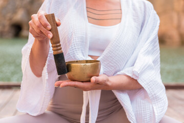 Woman practicing sound healing meditation with tibetan singing bowl outdoors
