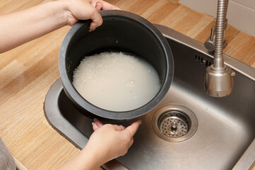 Person washing sticky rice in a pot under the sink, squeezing and cleaning it with water, part of food preparation in the kitchen