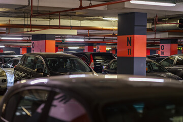 Car Parking Lot. Underground parking garage filled with parked cars and red labeled pillars in dim...