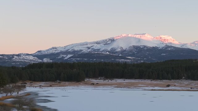 Smooth panoramic movement at Laguna La Zeta on frozen lake and forest side with distant glowing mountain peaks, Esquel, Province of Chubut, Argentina.