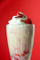 Milkshake with berry topping and foam on red background