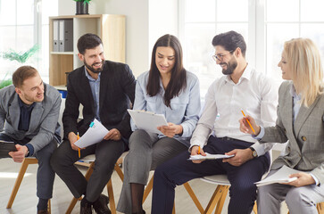 Group of cheerful young business people sitting in a row and talking with each other preparing for...