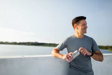 Man enjoying a sunny day by the water while holding a water bottle and smiling