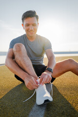 Man tying shoelaces while preparing for outdoor exercise during sunrise near a tranquil water body