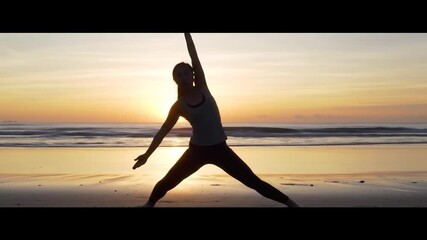 Woman silhouetted in a yoga pose on a sandy beach at sunrise
