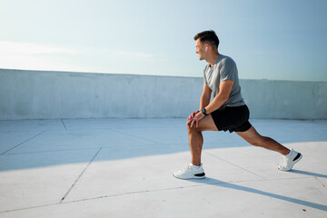 Man performs a stretching exercise on a rooftop during early morning sunlight for fitness and wellness