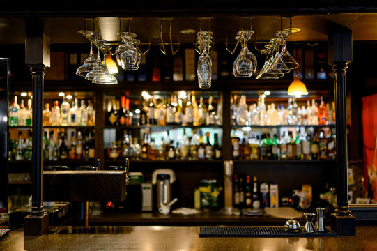 a bar counter with shelves filled with various bottles of alcohol and glasses hanging above it.