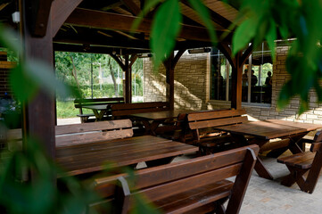 Wooden table and benches under a canopy, surrounded by greenery.