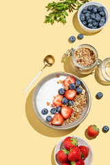 Natural yogurt with granola, blueberry and strawberry in a bowl on a yellow background