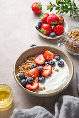 Natural greek yogurt with granola, blueberry and strawberry in a bowl on a light background