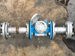 Close-up of a commercial water meter connected to stainless steel pipelines, showing flow...