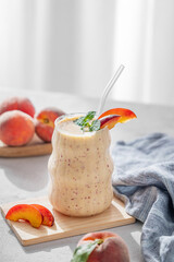 Smoothie with peach and banana in a glass on a light background near window with tropical fruit slices