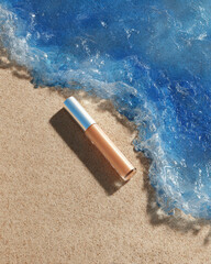 Sleek tube of foundation lies on soft, wet sand, with vibrant blue ocean waves gently lapping at shore, creating serene and inviting beach scene