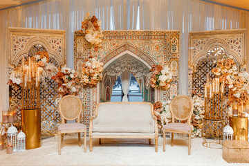 Luxurious wedding stage with Arabic style decor. Indian style wedding stage and interior decor with oriental painted arches, candles, sofa, flowers in gold colors. Elegant Islamic wedding stage design