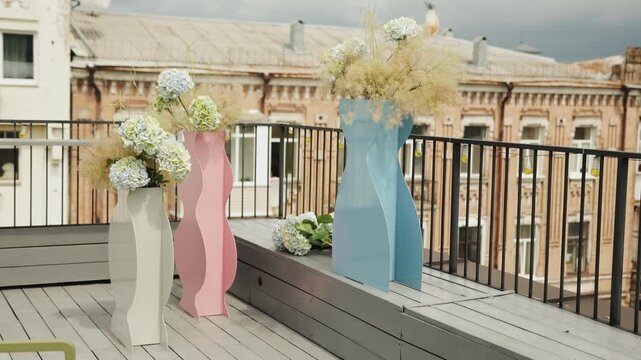 Wedding decoration of a wooden terrace of a restaurant. Modern large vases with beautiful bouquets of flowers on a bright ceiling. Decor for a restaurant, wedding or event.