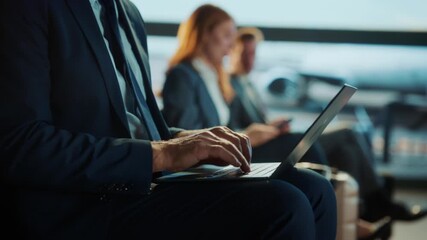 A businessman in a suit works on a laptop while sitting, blurred background with other business people. - Powered by Adobe