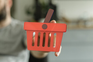 Fototapeta premium Red shopping cart icon held in hand. Perfect for e-commerce, online retail, and shopping themes.