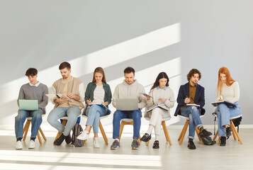 Young people with backpacks, notebooks and laptops sitting in lobby. Male and female fresher or...