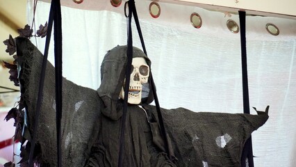 Halloween decoration representing a scary monster with a skull face and a black cloak hanging from...