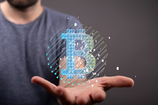 Image of a man's hand presenting a futuristic, holographic Bitcoin symbol. Perfect for cryptocurrency, finance, and technology concepts.