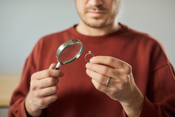 Unrecognizable man jeweler examining ring with magnifying glass, analyzing details, posing in...
