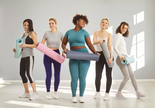 Indoor shot of five different women posing with fitness mats, being in good mood before training, do regular physical exercise in gym, dressed in activewear, isolated over grey background