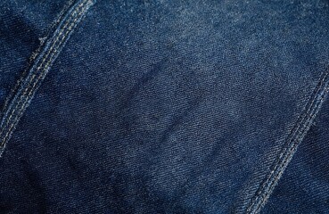Fototapeta premium Detailed close-up texture of dark blue denim jeans fabric. Features visible stitching detail on material surface. Cotton textile offers durable casual wear, classic western style for apparel,