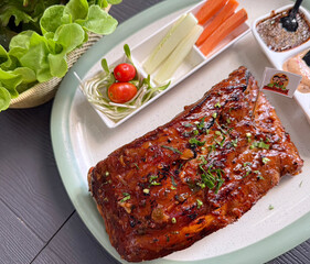 Top view of grilled pork ribs with barbecue glaze served with fresh vegetables and dipping sauce on...
