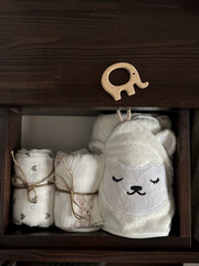 Muslin diapers, a white terry towel in the drawer of the bedside table. A wooden elephant teether is lying on the bedside table. Children's minimalistic accessories for a newborn
