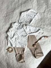 A set of neutral beige children's clothes for discharge. Baby's turtleneck, pants, cap, elephant teether and beads on the bed. Top view